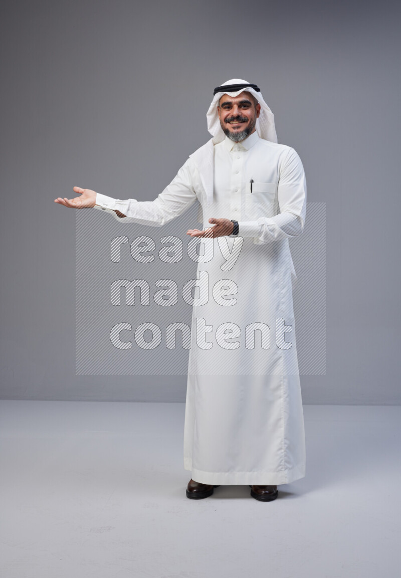 Saudi man Wearing Thob and white Shomag standing interacting with the camera on Gray background