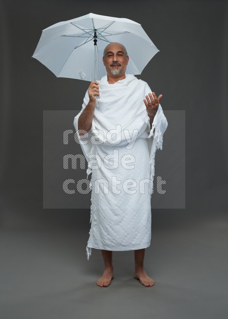 A man wearing Ehram Standing holding umbrella on gray background