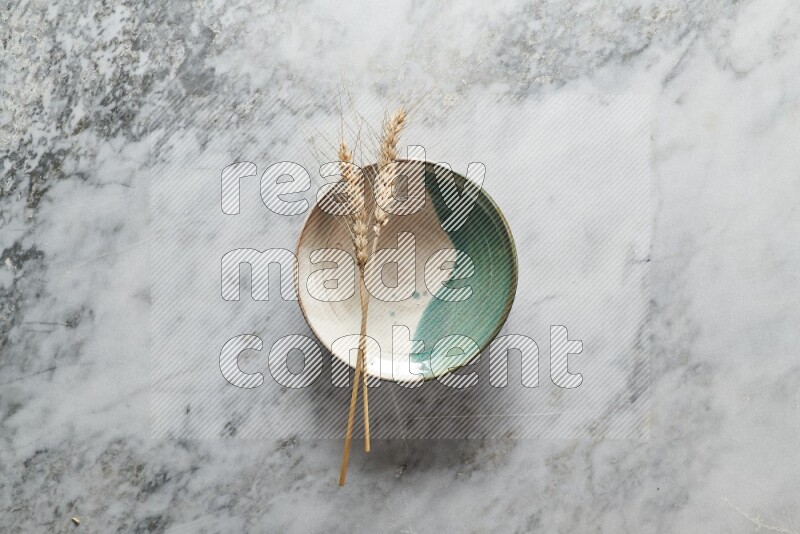 Wheat stalks on multicolored pottery plate on grey marble background