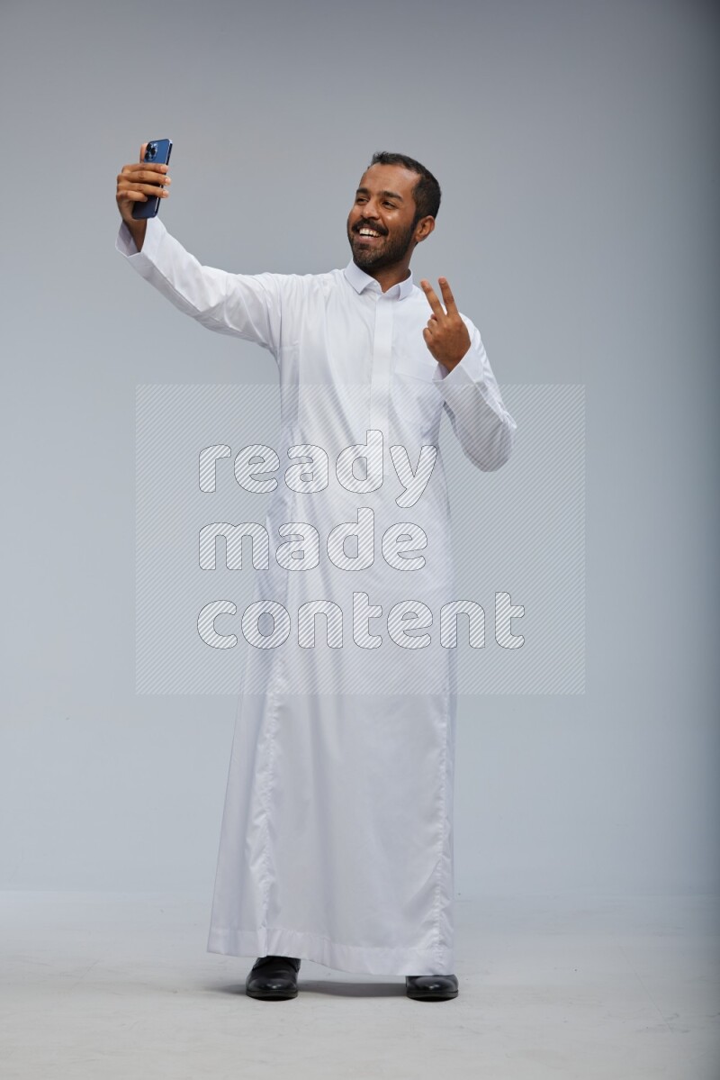 Saudi man wearing Thob standing taking selfie on Gray background