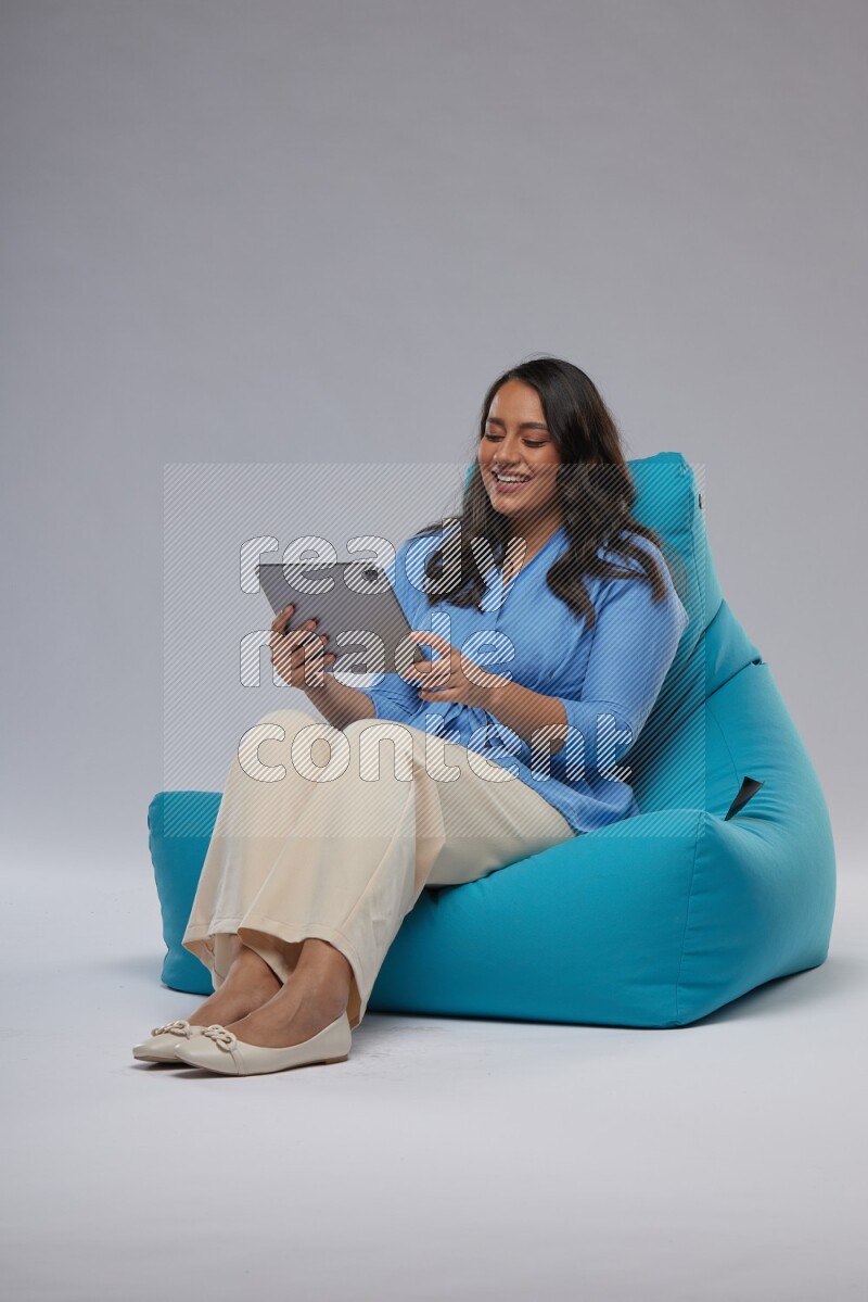 A woman sitting on a blue beanbag and working on tablet