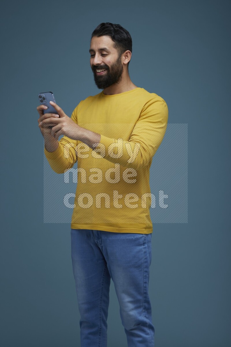 Man typing on his phone in a blue background wearing a yellow shirt
