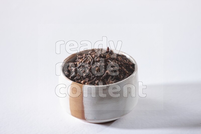 A beige ceramic bowl full of cloves on a white flooring