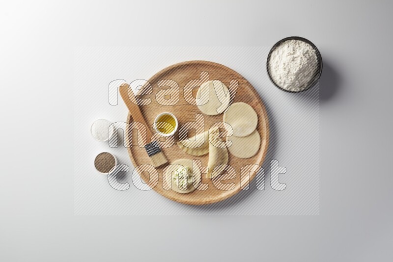two closed sambosas and one open sambosa filled with cheese while flour, salt, black pepper and oil with oil brush aside in a wooden dish on a white background