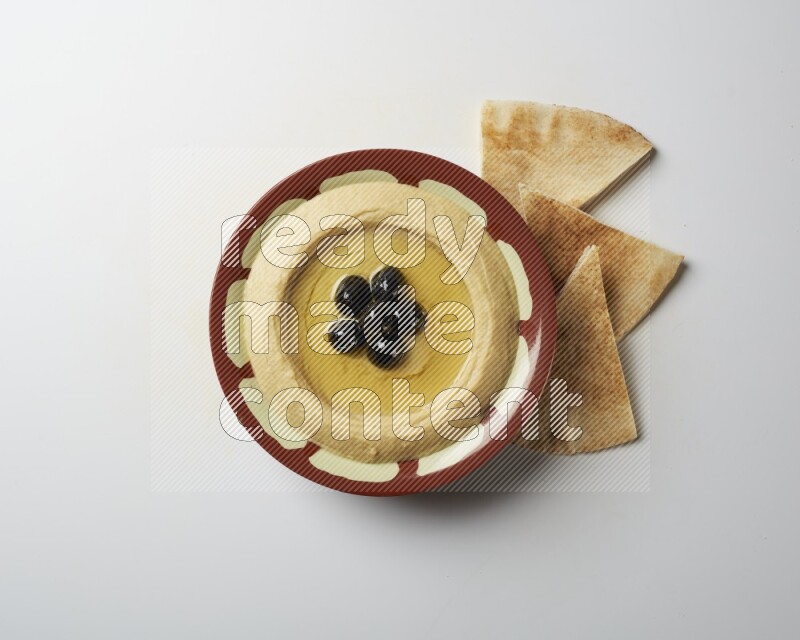 Hummus in a traditional plate garnished with black olives on a white background