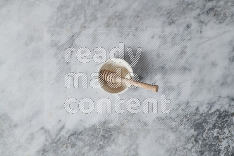 Beige pottery bowl with wooden honey dipper in it on grey marble background
