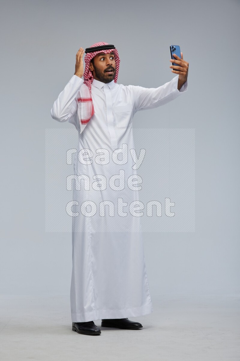 Saudi man Wearing Thob and shomag standing taking selfie on Gray background