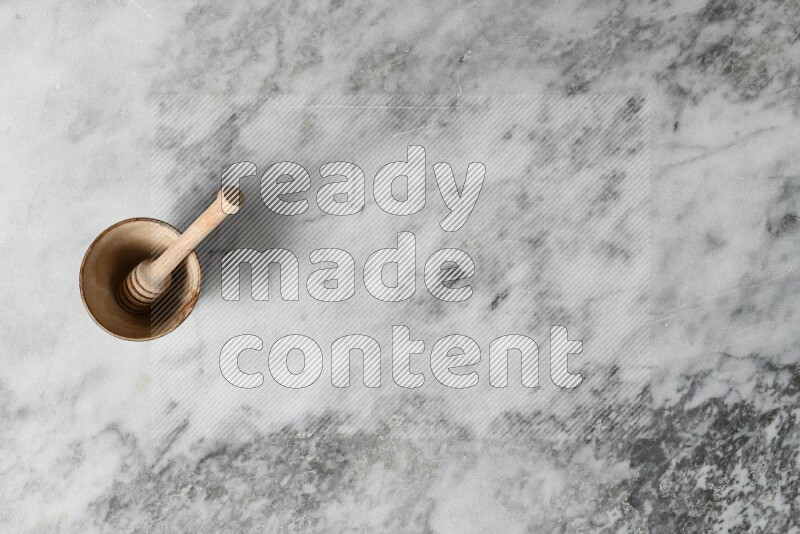 Beige pottery bowl with wooden honey dipper in it on grey marble background