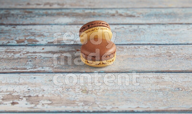 45º Shot of two Yellow and Brown Chai Latte macarons on light blue wooden background