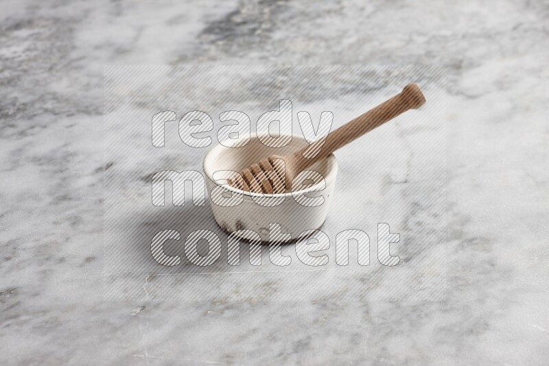 White pottery bowl with wooden honey dipper in it on grey marble background