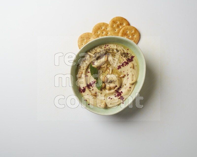 Hummus in a green plate garnished with zattar & sumak on a white background