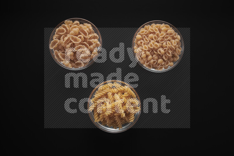Different pasta types in glass bowls on black background