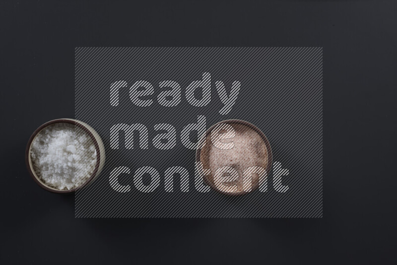 2 pottery bowls one is filled with himalayan salt and the other with white salt on black background