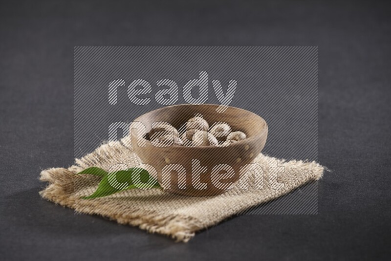 A wooden bowl full of whole nutmeg seeds on burlap fabric on a black flooring
