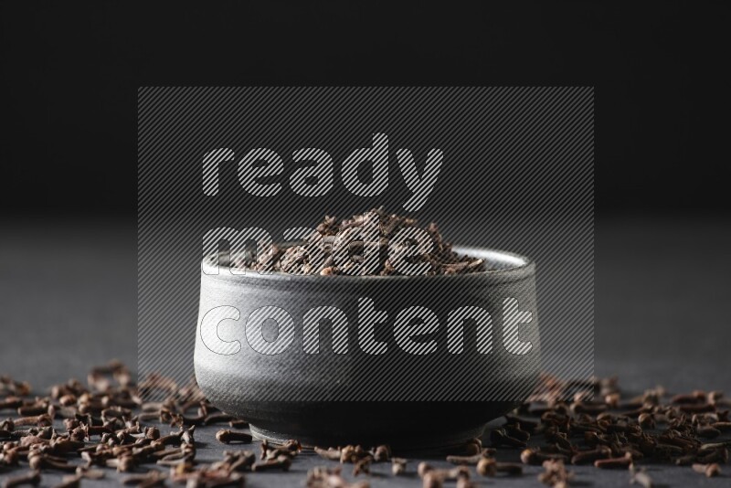 A black pottery bowl full of cloves on a black flooring