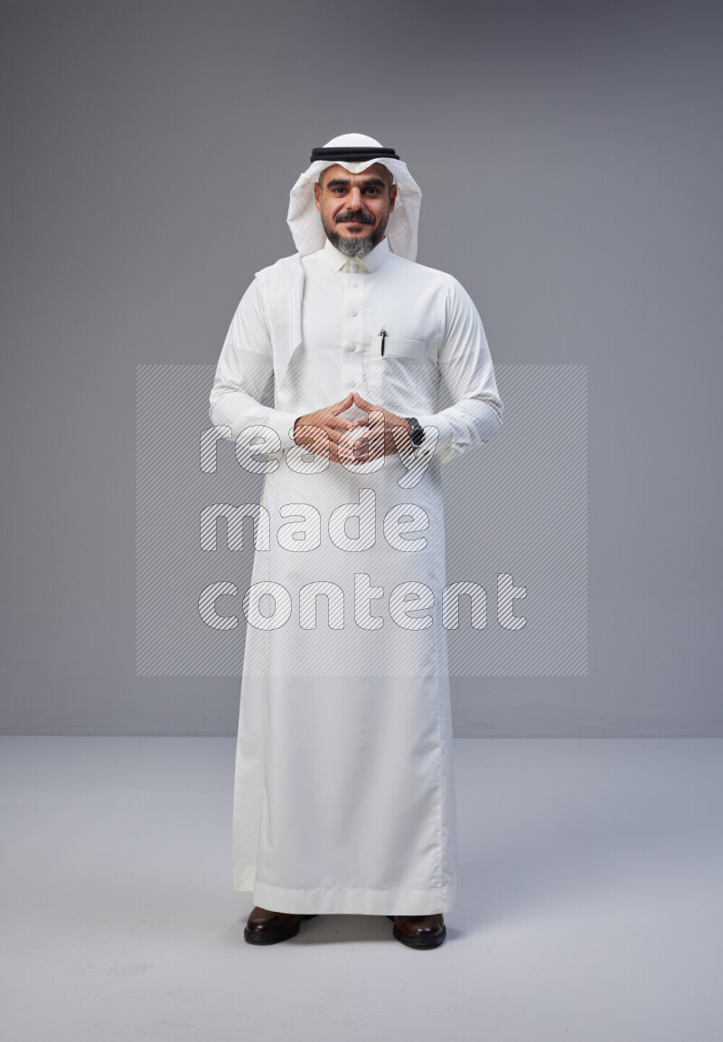 Saudi man Wearing Thob and white Shomag standing interacting with the camera on Gray background