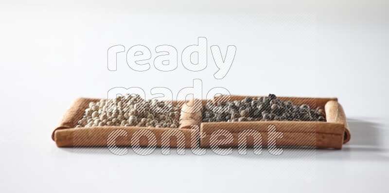 مربعان من أعواد القرفة ممتلئان بحبوب الفلفل الأسود والفلفل الأبيض علي خلفية بيضاء