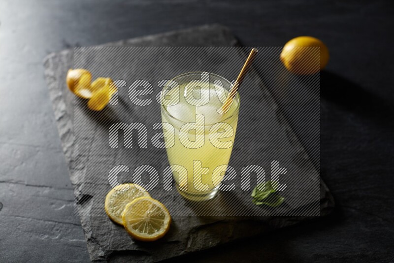 A glass of lemon juice with a straw on black background