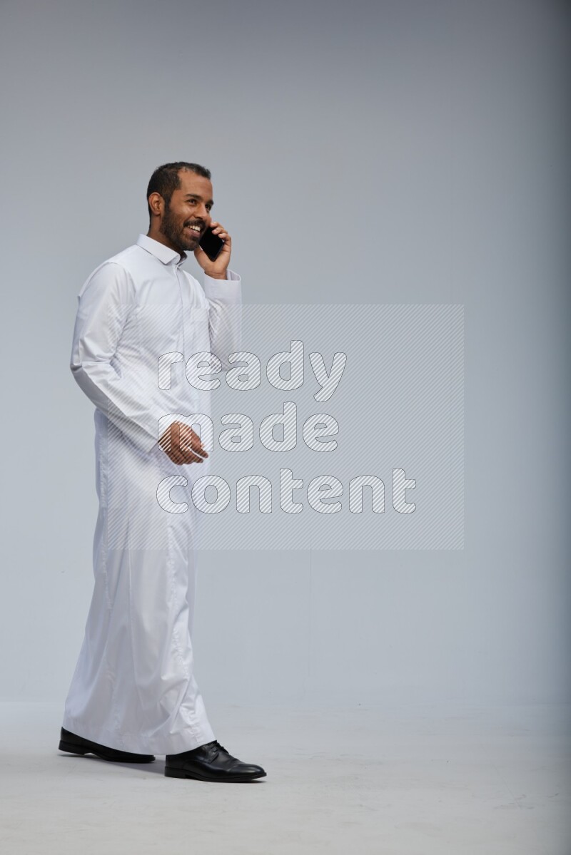 Saudi man wearing Thob standing talking on phone on Gray background