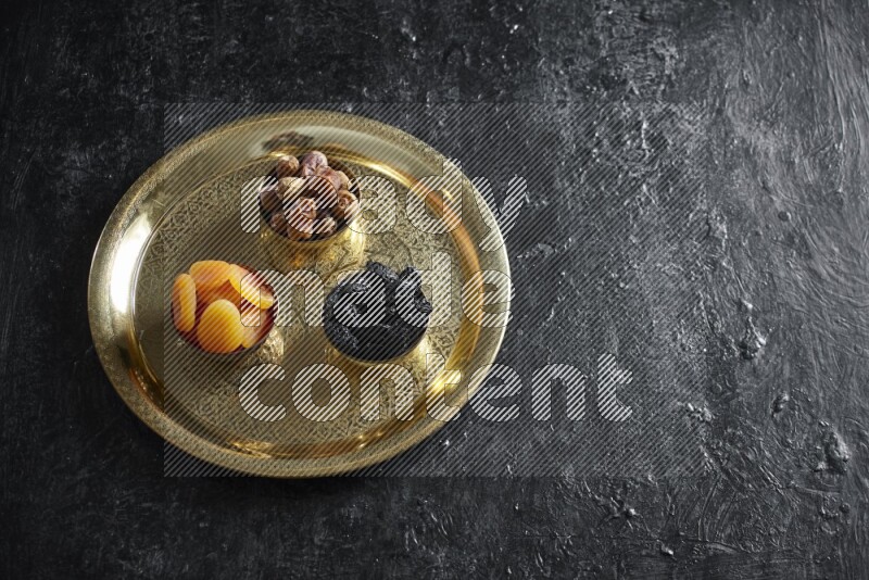 Dried fruits in metal bowls on a tray in a dark setup