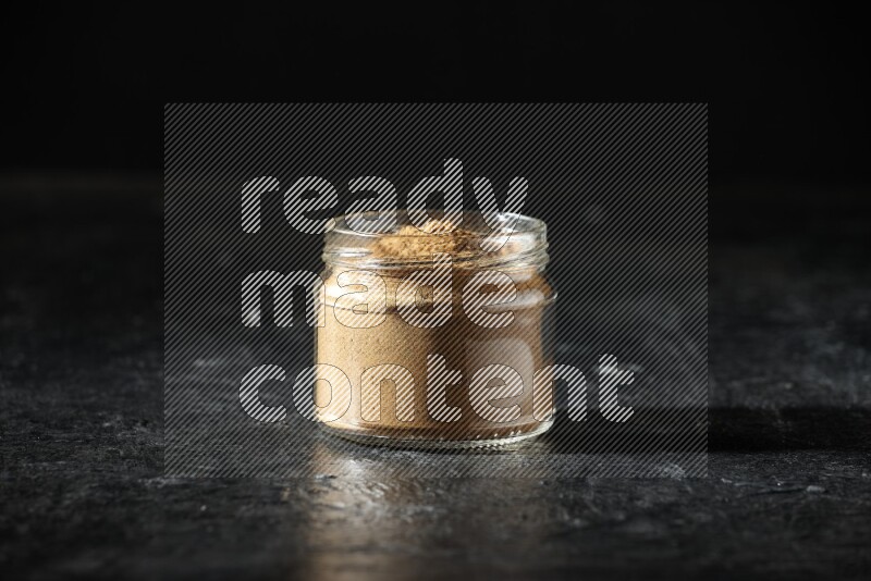 A glass jar full of allspice powder on a textured black flooring