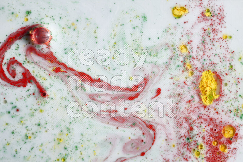 The image captures a splatter of yellow, red and green paint over a white backdrop