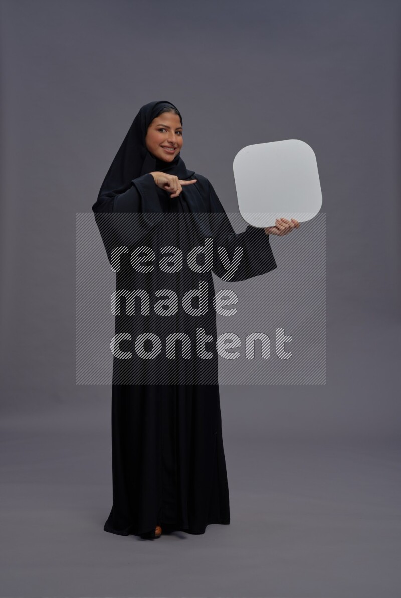 Saudi woman wearing Abaya standing holding social media sign on gray background