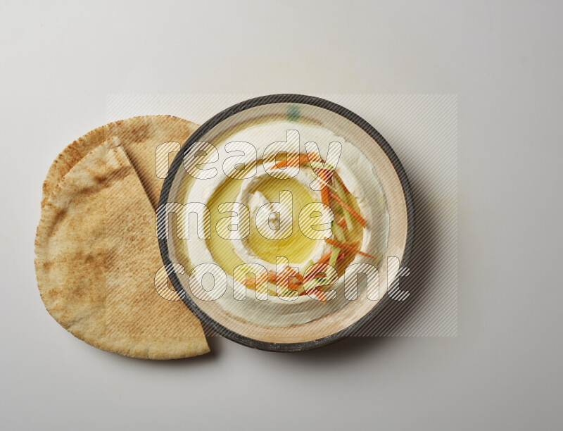 Lebnah garnished with sliced carrots &cucumber in a pottery plate on a white background