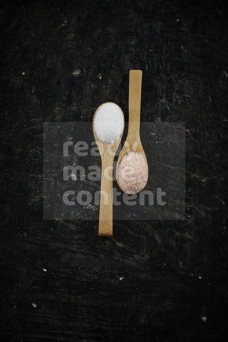 2 wooden spoons filled with fine and coarse salt on black background