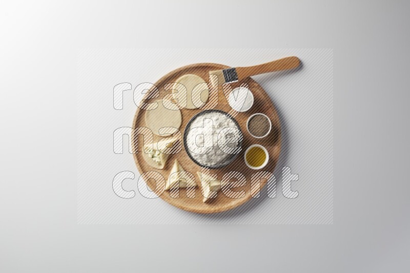 two closed sambosas and one open sambosa filled with cheese while flour, salt, black pepper and oil with oil brush aside in a wooden dish on a white background