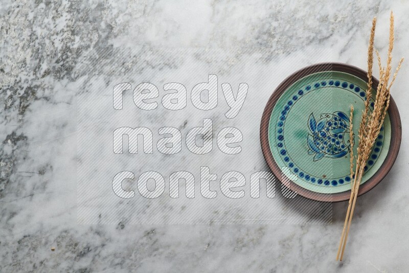 Wheat stalks on decorative pottery plate on grey marble background