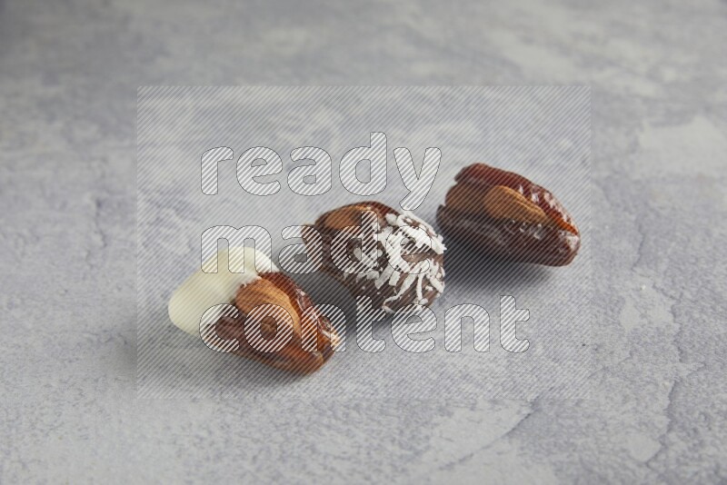 Three Almond stuffed dates plain and covered with chocolate on a light grey background