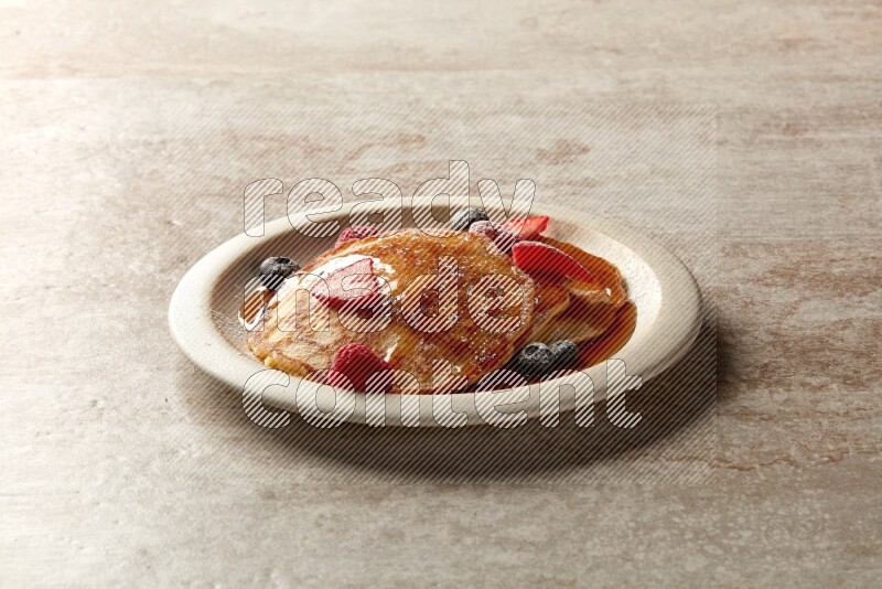 Three stacked mixed berries pancakes in a grey plate on beige background