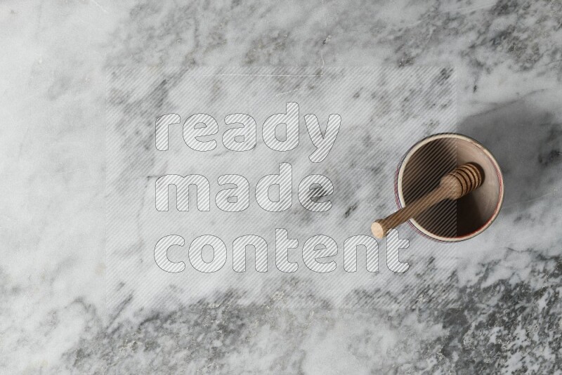 Beige pottery bowl with wooden honey dipper in it on grey marble background