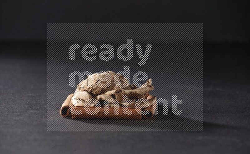 A single square of cinnamon sticks full of dried ginger on black flooring