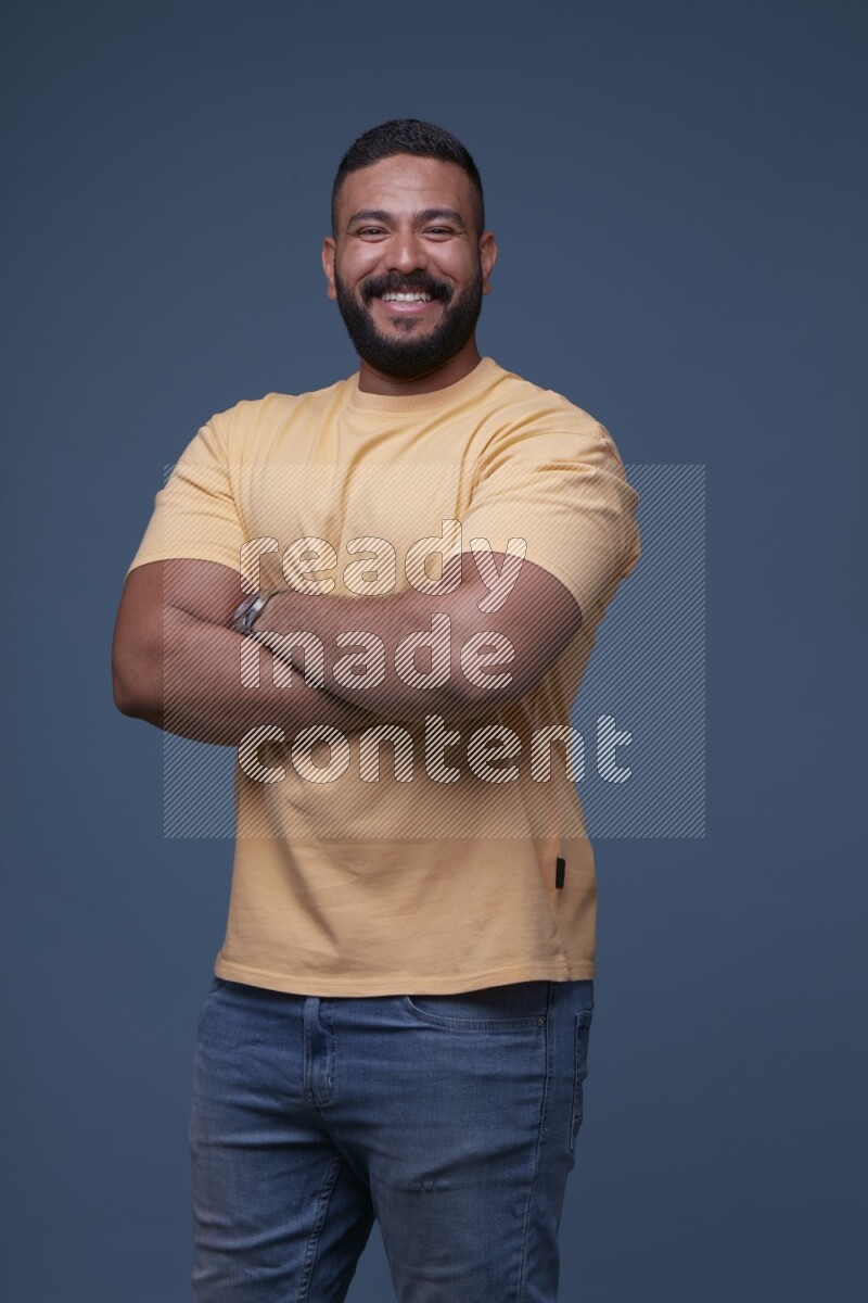 A man posing in a blue background wearing a yellow shirt