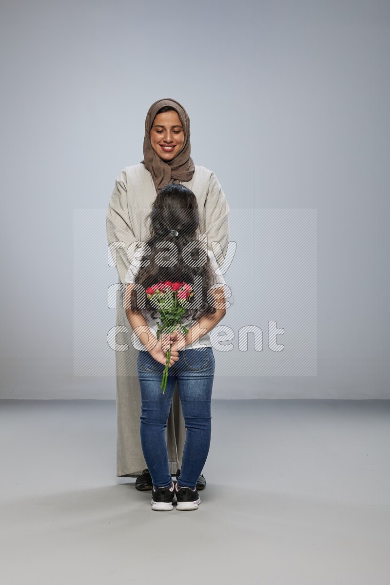A girl hiding a flower behind her back for her mother on gray background