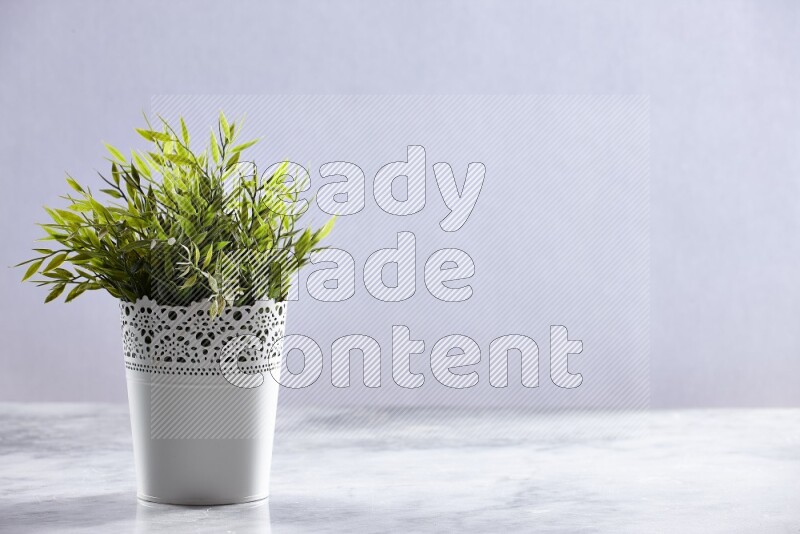 Green artificial plant in white decorative pot on grey marble background