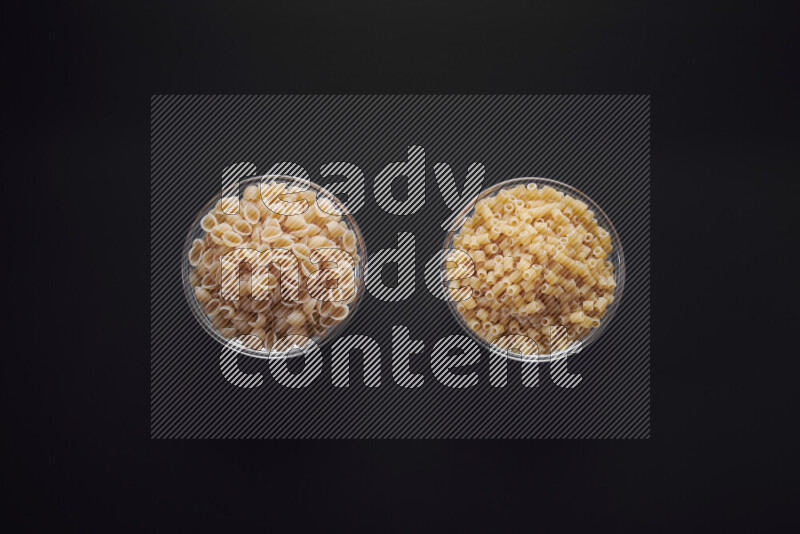 Different pasta types in glass bowls on black background