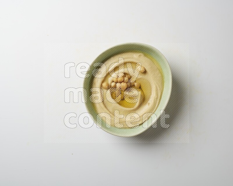 Hummus in a green plate garnished with roasted chickpeas  on a white background