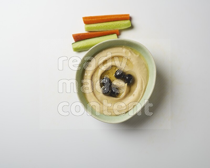 Hummus in a green plate garnished with black olives on a white background