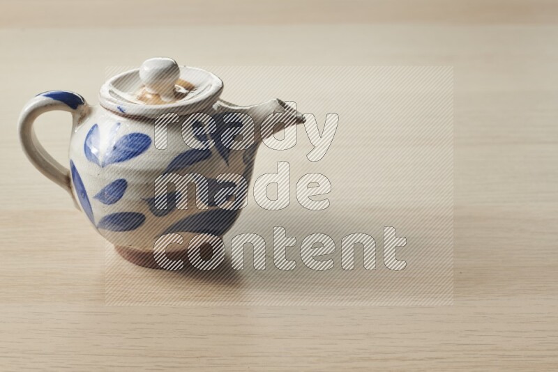 A pottery teapot on light wooden background