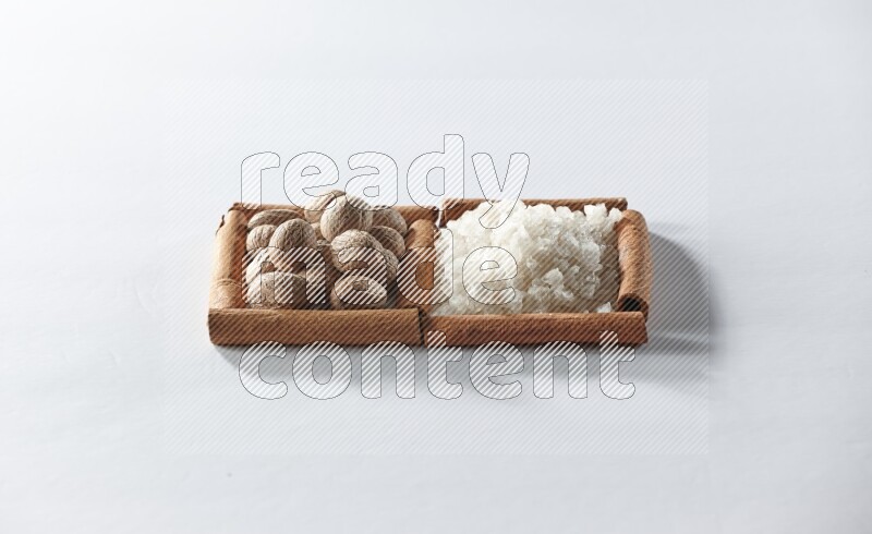 مربعان من أعواد القرفة ممتلئان بالملح الأبيض وجوزة الطيب علي خلفية بيضاء