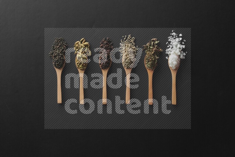 wooden spoons filled with white peppers, cloves, cardamom, salt, black peppers and basil on black flooring