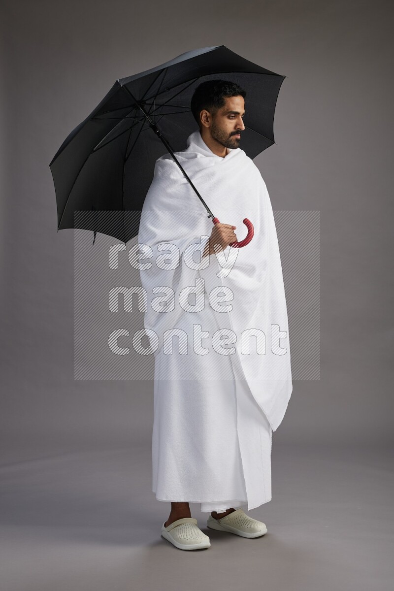 A man wearing Ehram Standing holding umbrella on gray background