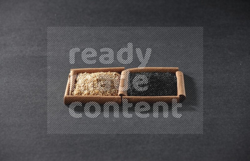 مربعان من أعواد القرفة ممتلئان ببذور السمسم وحبة البركة السوداء علي خلفية سوداء