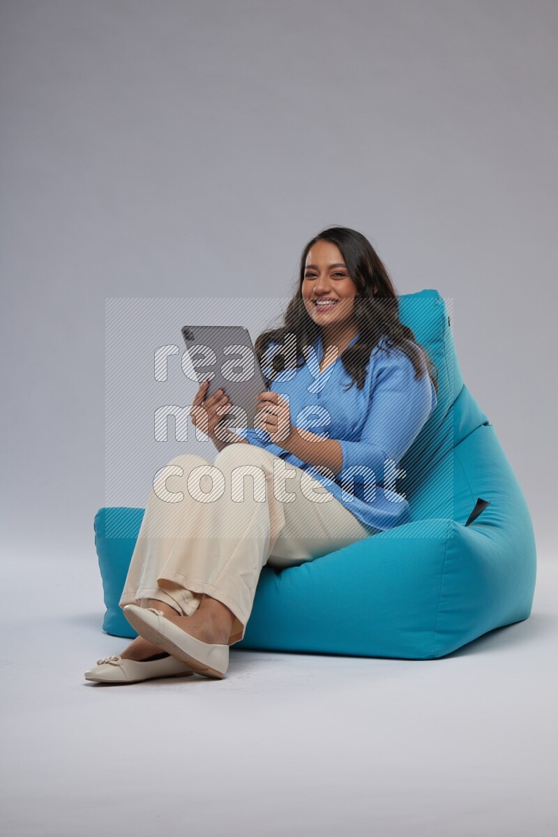 A woman sitting on a blue beanbag and working on tablet