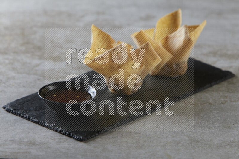 wonton cups with soy sauce ramkin on rectangle slate on grey textured counter top