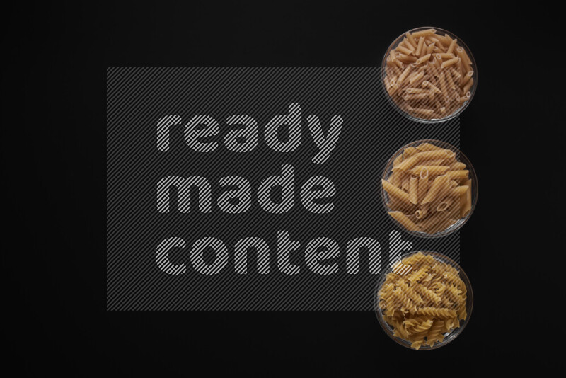 Different pasta types in 3 glass bowls on black background