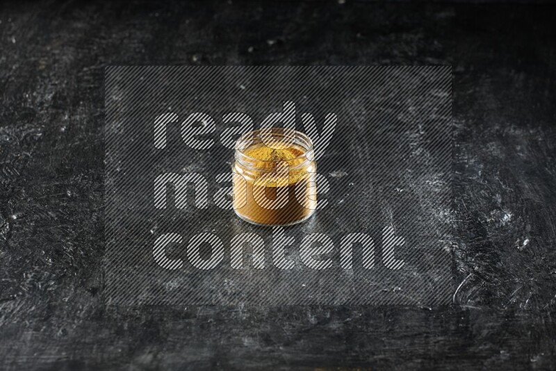 A glass jar full of turmeric powder on a textured black flooring